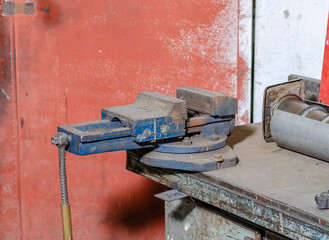 Old blue iron vise on a workbench workshop in a blurred environment of other equipment and tools, a special clamp for parts.
