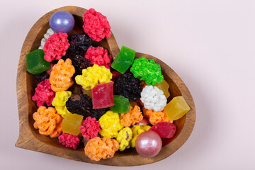 Colorful sweets and candies are poured into a heart-shaped wooden vase.