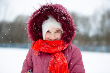 Child in winter. A little girl in a warm hat and hood looks at the camera and smiles.