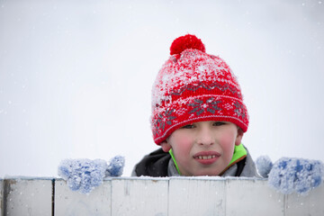 Child in winter. A little boy in a warm hat and mittens looks at the camera and smiles.