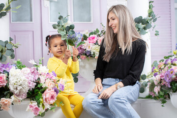 Multiethnic mom and daughter are sitting on the porch of the house. Cheerful mother with little daughter of African nationality. Family from different races.