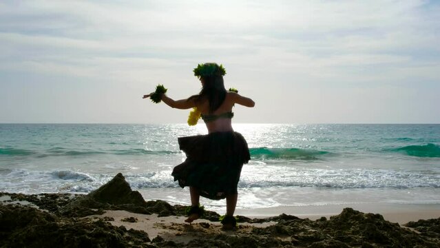 Hula dancer dancing hawaiian dance. Pretty and energetic woman performing hawaiian dancing on the beach with blanks. The perfect landscape. Woman dancing hula dance. Silhouette of woman dancing hula.