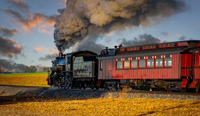 Fototapeta na wymiar A View of an Antique Passenger Steam Train Blowing Smoke Traveling Pass at Sunrise on a Beautiful Partly Cloudy Day