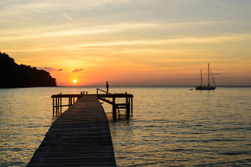 Obraz premium Unidentified man fishing on the wooden bridge pier which extends into the sea with beautiful sunset scenery landscape view of Bang Bao Beach, Koh Kood, Trat, Thailand.