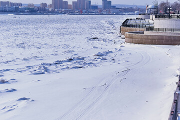 State border between Russia and China in winter. The Amur River under ice. Border trails. Cracks, snowmobile tracks. The embankment of Blagoveshchensk and the city of Heihe in the background. Sunlight