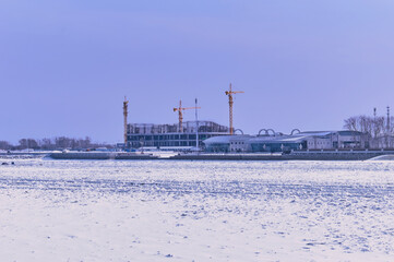 Fototapeta na wymiar View of the construction of the Chinese terminal of the international cable car from the Russian bank of the Amur River. February 2022. Snow and border barriers on ice. Blue purple morning sky.