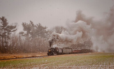 View of an Antique Steam Passenger Train Traveling in a Snow Storm that Just Started on a Winter Day