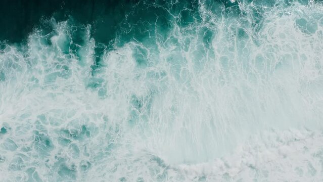 zoom out on the big power ocean waves with white wash. Aerial top view footage of fabulous sea tide on a stormy day. Drone filming breaking surf with foam in the Indian ocean. Big swell in Bali.