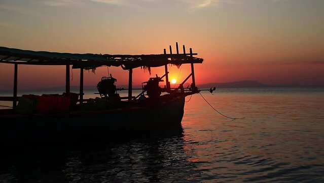Cinematic scenery of the sun during sunset being framed by the silhouette of a fishing boat off the coast of the touristic Rabbit Island or Koh Tonsay in Kep, Cambodia