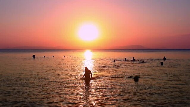 Silhouettes of people swimming and enjoying the warm sea while bathe in the summer sunset in Koh Tonsay or Rabbit Island in Kep, Cambodia