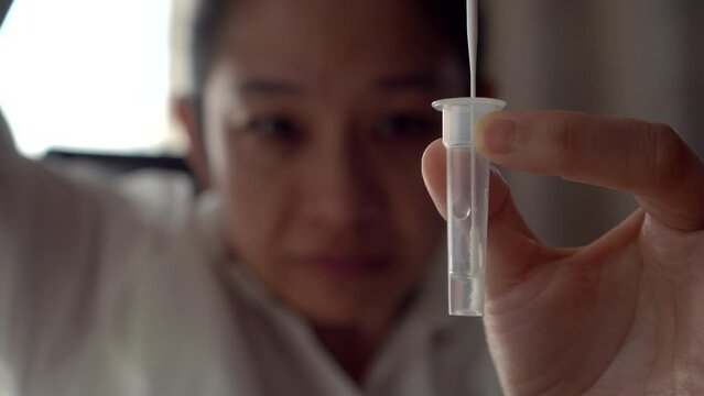 Asian woman do Covid ATK antigen nasal self test kit mixing liquid from nose with antigent in tube