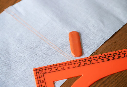 Work tools of a tailor. Photo of cut out piece of fabric with marking symbols on it, triangle ruler and a piece of chalk