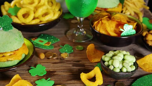 St Patrick`s holiday party invitation, bar menu background. Irish St Patrick`s day beer, ale glasses, snacks, appetizer, green burger, wooden bar table with shamrock, clover, coins, leprechaun hat 