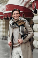  Young man wearing coat walking in the street. Young bearded guy with modern hairstyle in urban background