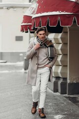 Young man wearing coat walking in the street. Young bearded guy with modern hairstyle in urban background