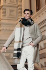 Young man wearing coat walking in the street. Young bearded guy with modern hairstyle in urban background