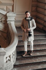  Young man wearing coat walking in the street. Young bearded guy with modern hairstyle in urban background