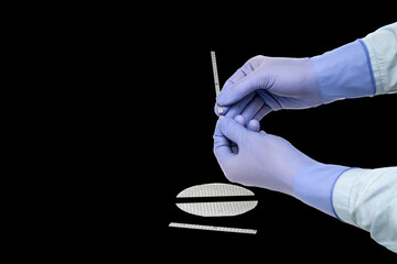 Hands in rubber gloves break multilayer semiconductor silicon wafer with a microcircuit chip of a...