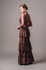 Vintage evening dress. Elegant classic brown gown. Brunette lady posing in studio. Full length...