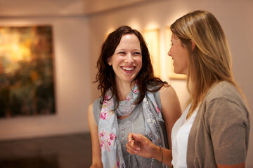 I dont get it either. Two young women share a laugh together while attending an art exhibition.