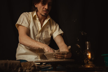 man in pottery workshop makes plate of clay, an authentic atmosphere, yellow lamp, lifestyle, magical atmosphere. Concept with your own hands, home entertainment. portrait
