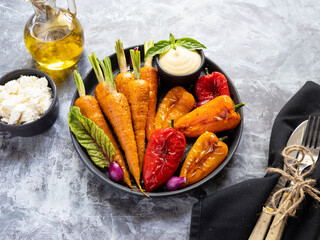 baked roast baby carrots, bell pepper in a plate, basil and spices vegan dish close up, white sauce, close up