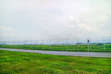 Road Outside Airport Lined by a Wire Fence with green grass and brigth sky