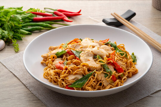 Spicy stir fried instant noodle with sliced chicken breast and thai basil leaves in white plate