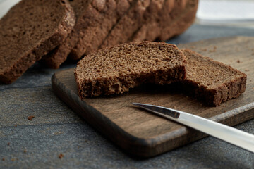 A piece of rye bread broken into two pieces on a wooden board. Sliced rye bread in the background
