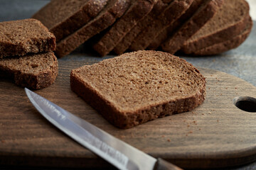 A piece of rye bread on a wooden board. Sliced rye bread in the background