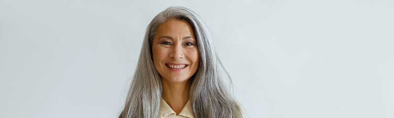 Portrait of smiling Asian woman with long hoary hair and crossed arms standing on light grey...