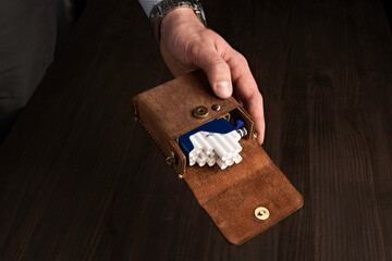 A man holds in his hand a close-up of an open cigarette case made of brown leather with cigarettes...