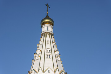 The high gabled roof of a Christian church with a gilded dome and a cross against a blue sky