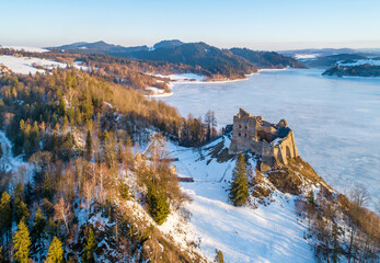 Artificial frozen Czorsztyn Lake on Dunajec River with ruins of medieval Czorsztyn castle and far view of Niedzica castle on the other side of the lake. Aerial view in winter in sunset light