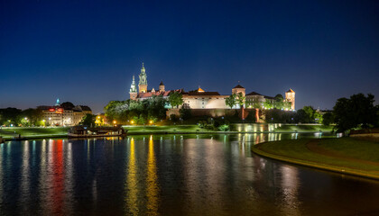 Plakat Poland, Krakow. Illuminated royal Wawel castle and cathedral at night and light reflections in Vistula River. Riverside with park, trees, promenade, lanterns, harbor and tourist ship