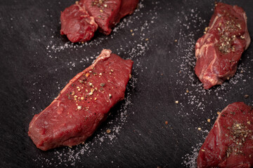 Raw beef tenderloin with salt and pepper on a black background, blackboard. Beef, game meat steaks. Red meat chops.