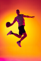 Fototapeta na wymiar Studio shot of muscled man, basketball player training with ball isolated on gradient yellow purple background in neon light. Beauty, sport, motion, activity concepts.