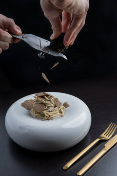 Faceless chef slicing truffles on pasta