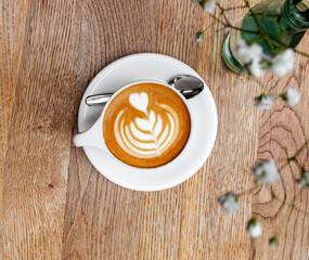 Cup of cappuccino on a wooden table with a small flowers.