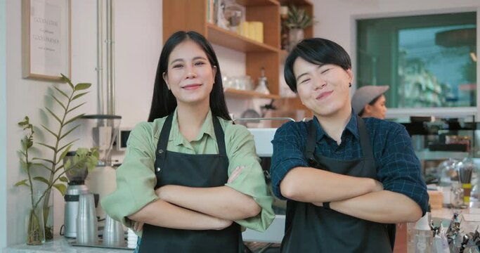 Couple Asian women wearing apron and stand in front of the counter In a coffee shop. Lesbian and tomboy couple owns and operates a cafe together. LGBTQ lifestyle