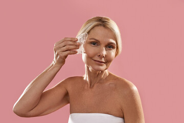 Fototapeta premium Mature caucasian woman apply ice slice on her face