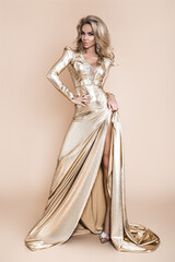 Elegant fashion. Stunning blonde woman in elegant long gold dress and perfect hairstyle on beige...