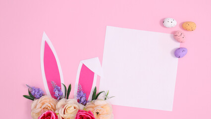 Spring holidays creative paper card copy space with bunny ears decorated with bloom flowers on pastel pink background. Creative Easter concept