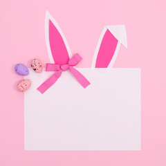 Romantic elegant paper card copy space with bunny ears and Easter eggs on pastel pink background. Flat lay minimal