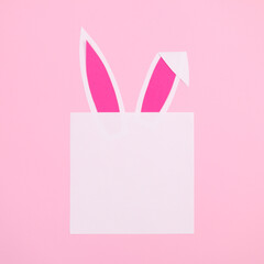Creative paper card copy space with bunny ears on pastel pink background. Flat lay Easter greeting card idea. Minimal concept