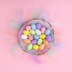 Creative Easter pastel bright pink background with rainbow feathers and colored eggs in wooden basket. Flat lay minimal. Spring holidays concept