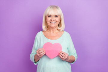 Photo of cheerful affectionate old lady hold pink heart shape card wear teal shirt isolated violet color background