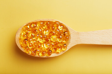 Vitamin D3 Capsules in a spoon with other vitamin D3 capsules around them on a yellow background