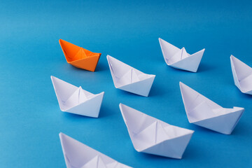 Business Leadership Concept - Orange Color Paper ship Origami leading the rest of the white paper ship on blue background.