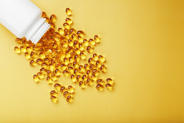 Golden Omega-3 fish oil capsules poured out of a jar on a yellow background